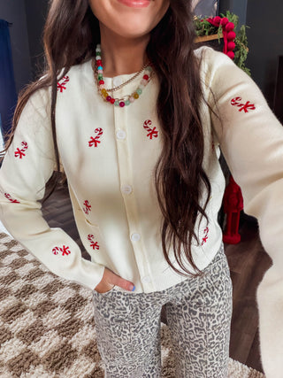 A woman wearing a cream-colored knit cardigan with red embroidered candy cane motifs, paired with gray leopard-print pants and a colorful beaded necklace.
house of color Autumn
house of color Spring
shop by color season